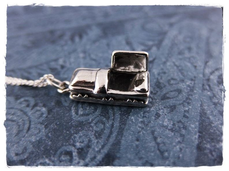 May include: A silver charm necklace featuring a small, open coffin pendant. The coffin is detailed with a hinged lid and a textured surface.