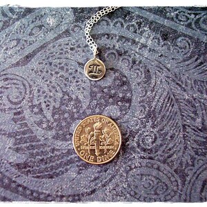 May include: A silver necklace with a charm that says "II" on a dark blue background with a paisley pattern. A US dime is also visible in the image.