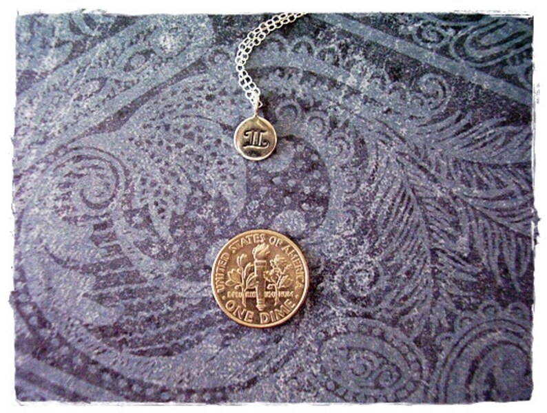 May include: A silver necklace with a charm that says "II" on a dark blue background with a paisley pattern. A US dime is also visible in the image.