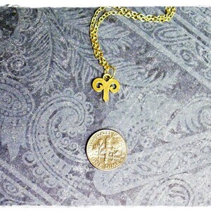 Peut inclure: Un collier en cha&icirc;ne dor&eacute;e avec un pendentif b&eacute;lier en or. Le collier est pos&eacute; sur une surface &agrave; motifs gris.