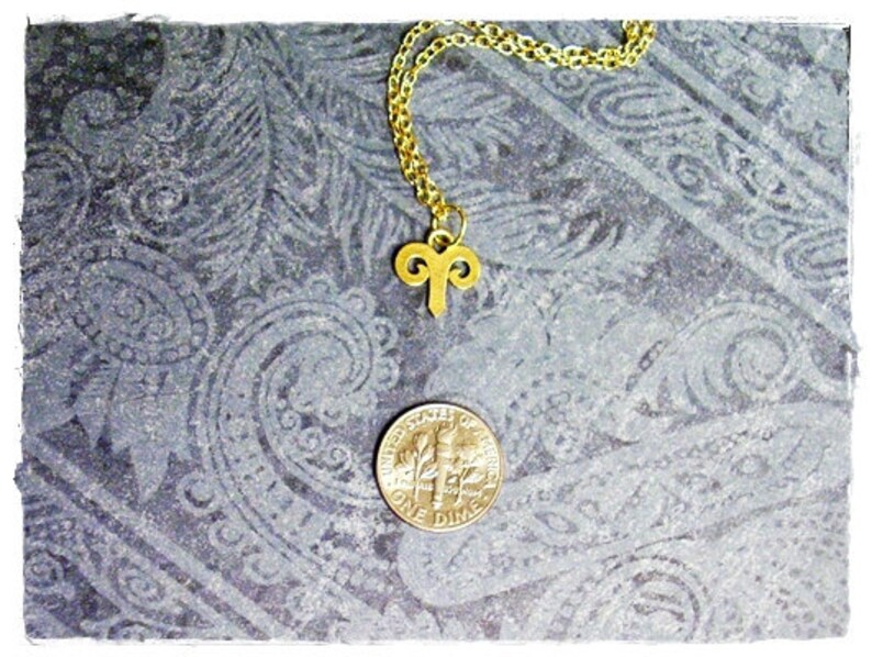 Peut inclure: Un collier en cha&icirc;ne dor&eacute;e avec un pendentif b&eacute;lier en or. Le collier est pos&eacute; sur une surface &agrave; motifs gris.