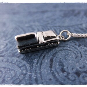 May include: A silver charm necklace featuring a miniature silver sleigh pendant. The sleigh has a detailed design with a curved roof and a small seat.