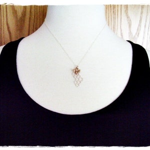 May include: A silver necklace with a honeycomb pendant and a small bee charm. The necklace is worn by a person wearing a black tank top.