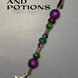 May include: A purple and green beaded hair clip with a silver witch hat charm. The clip says "Spells and Potions" at the top.