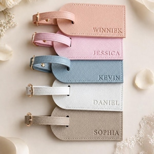 May include: Five rectangular luggage tags with gold-tone buckles and textured surfaces in peach, light pink, dusty blue, white, and taupe. Each tag is embossed with a name: WINNIEK, JESSICA, KEVIN, DANIEL, and SOPHIA, arranged in a vertical stack.
