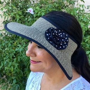 May include: A black and white polka dot flower adorns a wide-brimmed sun hat with a black band. The hat is made of a woven straw material.