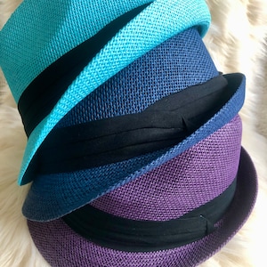 May include: Three straw hats stacked on top of each other. The top hat is light blue, the middle hat is dark blue, and the bottom hat is purple.