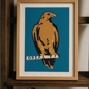 Op de afbeelding: Een ingelijste kunstdruk met een gestileerde illustratie van een gouden adelaar op een blauwe achtergrond. De adelaar zit op een tak, met de tekst "OPEA". De print zit in een lichte houten lijst en wordt tentoongesteld op een donkere houten plank.