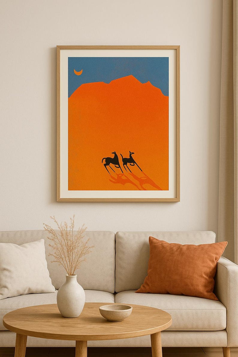 May include: Framed art print featuring a minimalist desert landscape. The artwork depicts two black animals with long shadows against an orange background, a blue sky, and a crescent moon. The print is in a wooden frame.