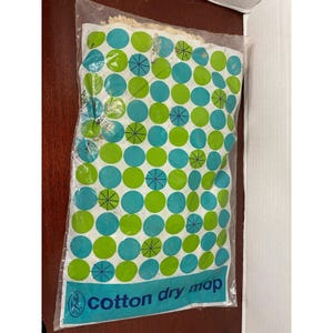 May include: A cotton dry mop head packaged in a clear plastic bag. The packaging features a repeating pattern of lime green and turquoise circles, some with dark blue starburst accents. The text "cotton dry mop" is printed in blue at the bottom.