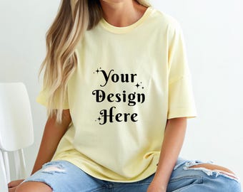 May include: A light yellow t-shirt with the text "Your Design Here" in black script. The shirt is a relaxed fit and is paired with blue jeans. The image is a lifestyle shot, showcasing the t-shirt's design.