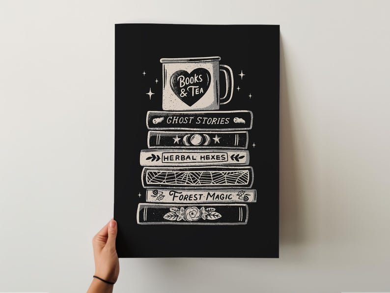 May include: Black and white art print showing a stack of books with titles such as "Ghost Stories" and "Forest Magic." A mug with a heart and the words "Books & Tea" sits on top. The print is held by a person.
