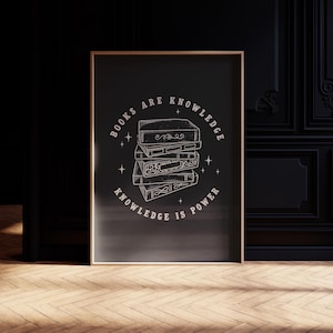 May include: A framed art print featuring a stack of books with the text "BOOKS ARE KNOWLEDGE, KNOWLEDGE IS POWER" in a circular design. The artwork is in white on a black background, with a gold frame.
