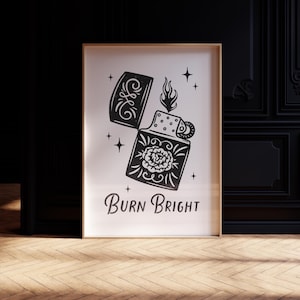 以下が含まれることがあります： 白黒の額入りアートプリント。ヴィンテージライターの詳細なイラストで、花の模様と「Burn Bright」の文字が描かれています。ライターは開いており、炎が出ています。