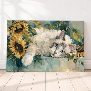 Op de afbeelding: Een canvas print met een witte en grijze kat met blauwe ogen, rustend tussen zonnebloemen en groene bladeren. Het kunstwerk is in een schilderstijl met zachte kleuren, wat een serene scène creëert. De kat is het centrale element van de afbeelding.