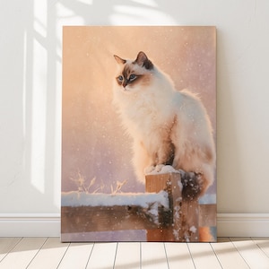 Peut inclure: Impression sur toile d'un chat blanc et beige duveteux aux yeux bleus, perché sur un poteau de clôture en bois enneigé. Le chat regarde vers la gauche, avec une douce lumière dorée en arrière-plan. L'œuvre évoque une scène hivernale.