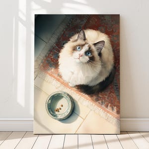 May include: A canvas print featuring a Ragdoll cat with striking blue eyes, looking upwards. The cat is positioned on a patterned rug, with a ceramic bowl containing food in the foreground. The artwork is set against a white wall.
