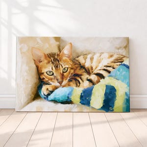 May include: A rectangular canvas print featuring an impressionistic painting of a brown tabby cat with green eyes resting on a blue and yellow striped blanket. The artwork displays visible brushstrokes and a textured appearance throughout the image.