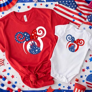May include: Red t-shirt and white onesie featuring a patriotic Minnie Mouse design. The design includes a bow, ears, and a castle silhouette filled with stars. The word "Name" is printed on the design.