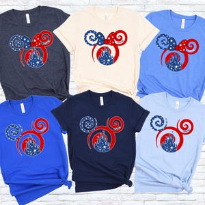 May include: A collection of six short-sleeved t-shirts in various colors, including navy, cream, blue, and light blue. Each shirt features a red, white, and blue graphic of Mickey Mouse ears with a castle silhouette.