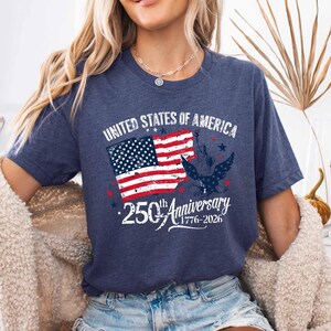May include: Navy blue t-shirt with a patriotic design. The graphic features the American flag, the Statue of Liberty, and an eagle, with the text "UNITED STATES OF AMERICA" and "250th Anniversary 1776-2026".