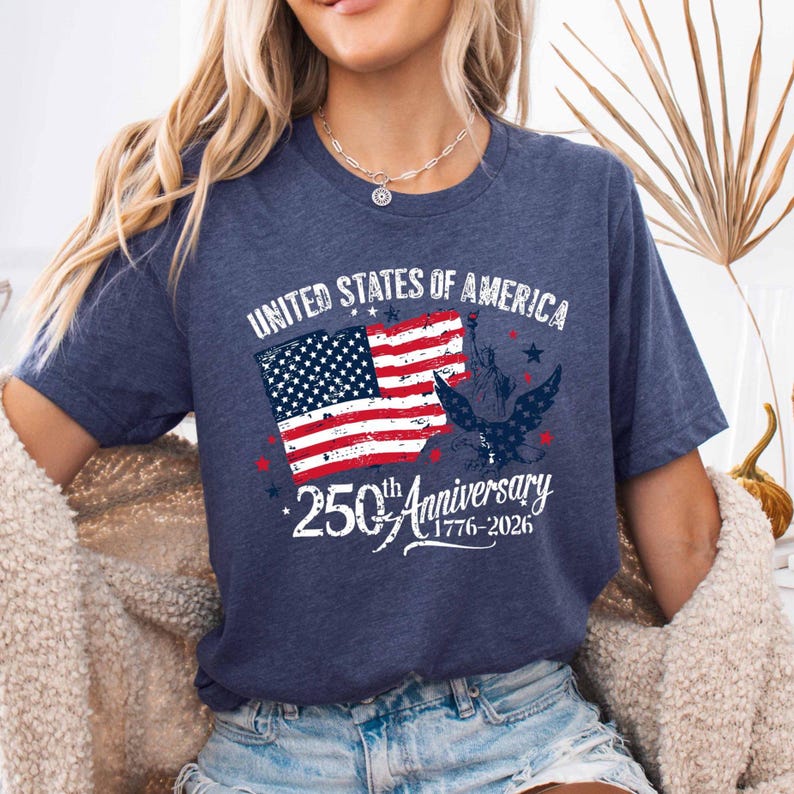 May include: Navy blue t-shirt with a patriotic design. The graphic features the American flag, the Statue of Liberty, and an eagle, with the text "UNITED STATES OF AMERICA" and "250th Anniversary 1776-2026".