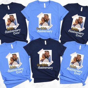 May include: A collection of short-sleeved t-shirts in various shades of blue. Each shirt features a printed image of a couple and the text "50th Anniversary Crew" or "Our 50th Anniversary". The shirts are likely for an anniversary celebration.