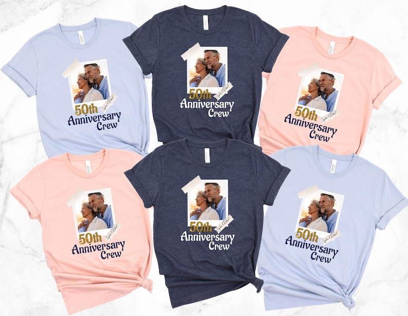 May include: Assortment of t-shirts in light blue, navy, and pink. Each shirt features a photo of a couple and the text "50th Anniversary Crew" in navy blue. The shirts are short-sleeved and have a crew neck.