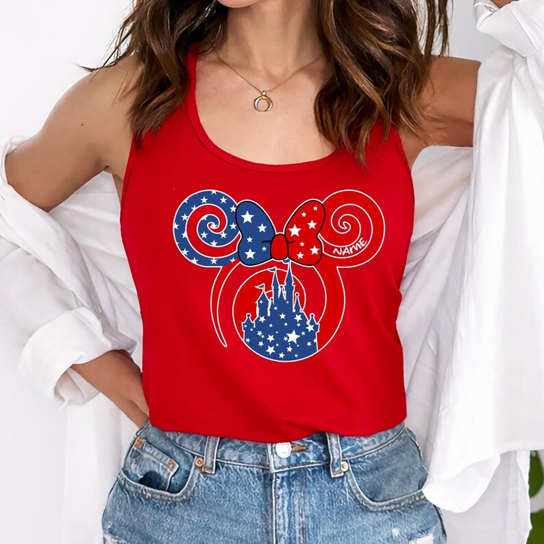 May include: Red tank top featuring a patriotic Minnie Mouse design. The design includes a bow with red and white stars, blue and white stars on the ears, and a blue castle silhouette. The word "NAME" is printed on the design.