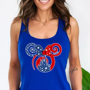May include: A royal blue tank top featuring a patriotic Mickey Mouse design. The design includes a red bow with white stars, a blue bow with white stars, and a white castle silhouette. The word "NAME" is written on the design.