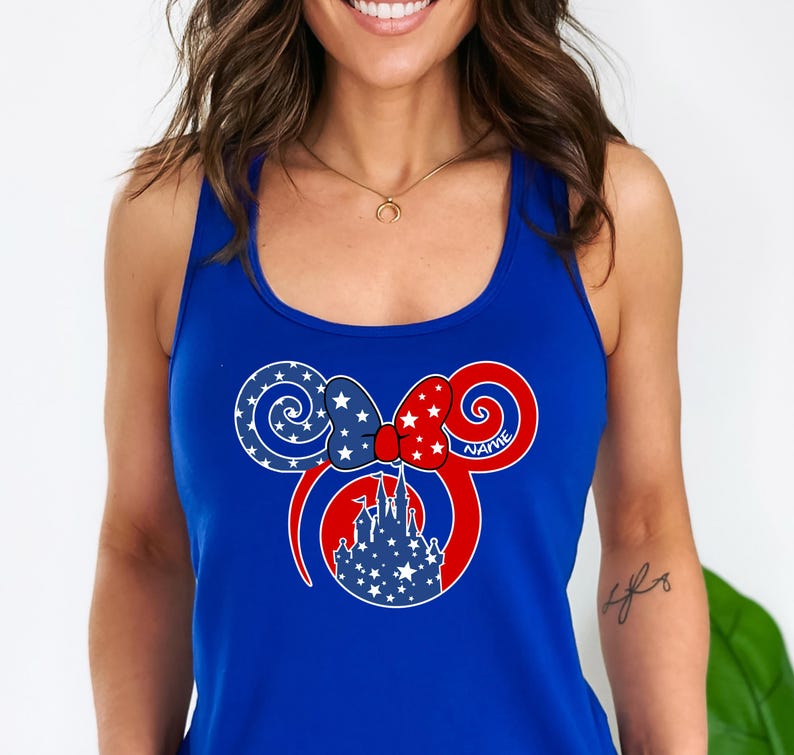 May include: A royal blue tank top featuring a patriotic Mickey Mouse design. The design includes a red bow with white stars, a blue bow with white stars, and a white castle silhouette. The word "NAME" is written on the design.