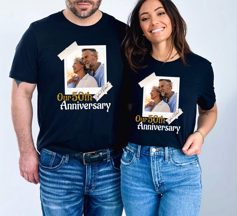 May include: Black t-shirts with a photo print and text. The photo shows an older couple. The text reads "Our 50th Anniversary" in gold script. The photo is taped to the shirt with white tape.