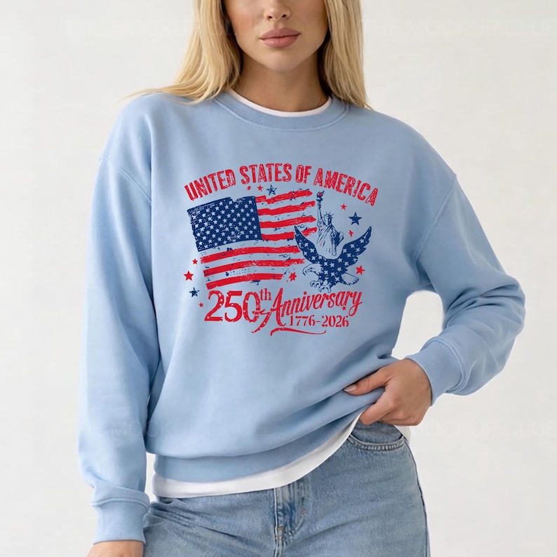 May include: Pale blue sweatshirt featuring a patriotic design for the 250th anniversary of the United States. The graphic includes the American flag, Statue of Liberty, and an eagle, with text reading "United States of America" and "250th Anniversary 1776-2026."