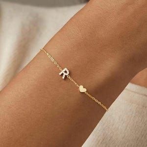 Könnte beinhalten: Eine weiße Keramik-Tasse mit schwarzem Henkel und dem Text "But First, Coffee" in fetter, schwarzer Schrift. Die Tasse steht vor einem verschwommenen Hintergrund, der eine gemütliche Umgebung suggeriert.