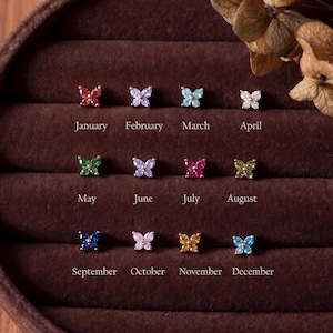 May include: Twelve butterfly-shaped stud earrings arranged in three rows, each featuring coloured stones representing birth months from January to December. The earrings are gold-toned with various gemstone colours including red, purple, blue, white, green, pink, and yellow.
