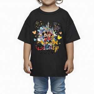 K&ouml;nnte beinhalten: Schwarzes T-Shirt mit einer bunten Grafik von Disney-Figuren, darunter Micky und Minnie Maus, vor einem Schloss. Der Text "Disney 2026" ist ebenfalls auf dem T-Shirt abgebildet. Das T-Shirt wird von einem Kind getragen.