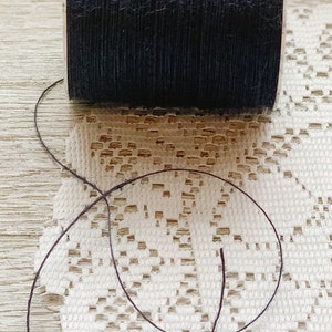 May include: A spool of black thread with a length of thread extending from the spool.