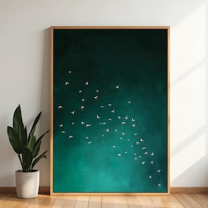 May include: A framed art print featuring a flock of white birds in flight against a teal and dark green background. The artwork is encased in a natural wood frame and leans against a white wall. A potted plant is visible in the foreground.