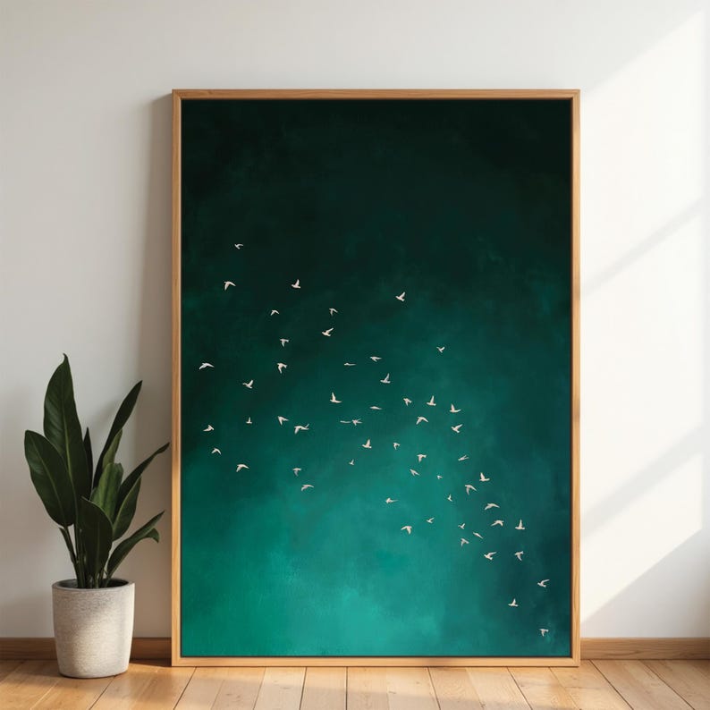 May include: A framed art print featuring a flock of white birds in flight against a teal and dark green background. The artwork is encased in a natural wood frame and leans against a white wall. A potted plant is visible in the foreground.