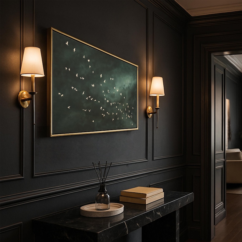 Op de afbeelding: Een donker, elegant interieur met een ingelijst kunstwerk met een zwerm vogels tegen een sombere groene lucht. De kamer heeft zwarte lambrisering, wandkandelaars en een console met marmeren blad met decoratieve items.