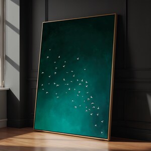 May include: A framed art print featuring a teal and emerald green background with a flock of white birds in flight. The artwork is displayed in a room with a wooden floor and a dark wall, and the frame is gold.