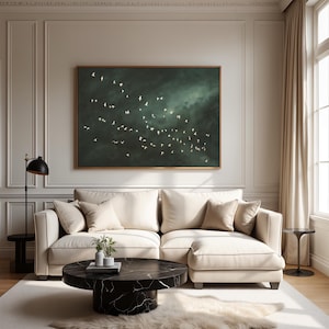Op de afbeelding: Een woonkamer met een groot, ingelijst kunstwerk dat vogels in vlucht tegen een donkere, bewolkte lucht afbeeldt. De kamer omvat een cr&egrave;mekleurige hoekbank, een zwarte marmeren salontafel en een decoratief tapijt.
