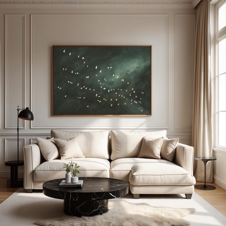 Op de afbeelding: Een woonkamer met een groot, ingelijst kunstwerk dat vogels in vlucht tegen een donkere, bewolkte lucht afbeeldt. De kamer omvat een cr&egrave;mekleurige hoekbank, een zwarte marmeren salontafel en een decoratief tapijt.
