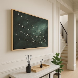 Op de afbeelding: Een ingelijste wandkunstprint met een zwerm witte vogels in vlucht tegen een donkergroene achtergrond. Het kunstwerk wordt getoond in een kamer met een witte muur en een houten lijst. Het thema is natuur en woondecoratie.