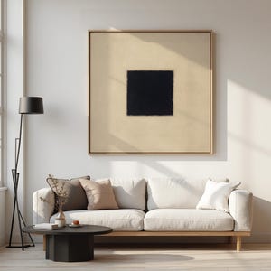 Könnte beinhalten: Ein weißes Sofa mit zwei Kissen steht vor einem beige gerahmten Gemälde mit einem schwarzen Quadrat in der Mitte. Eine schwarze Stehlampe steht links vom Sofa und ein schwarzer runder Couchtisch steht vor dem Sofa.