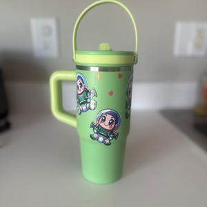 Puede incluir: Taza de viaje verde con asa y tapa. La taza tiene una imagen de dibujos animados de un personaje de la pel&iacute;cula Toy Story.