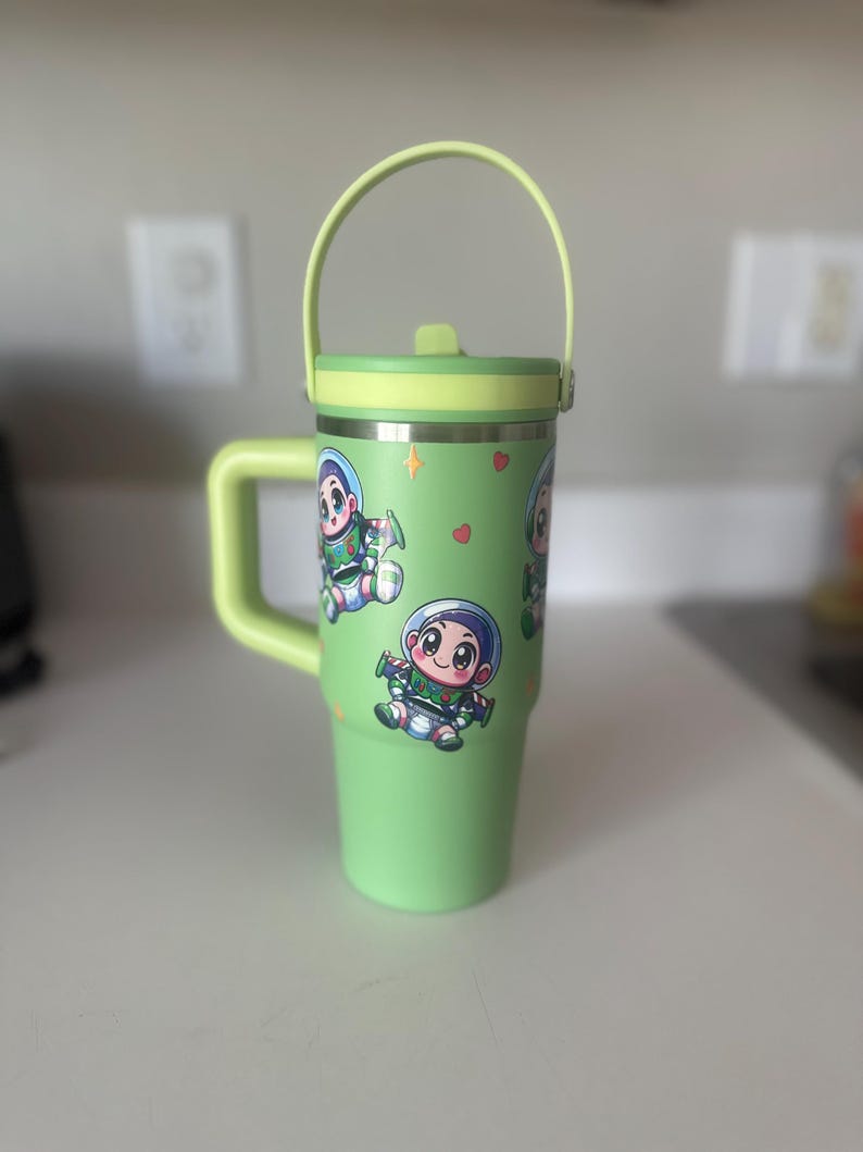 Puede incluir: Taza de viaje verde con asa y tapa. La taza tiene una imagen de dibujos animados de un personaje de la pel&iacute;cula Toy Story.