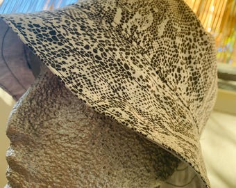 May include: A bucket hat with a black and white spotted pattern. The hat is made of a lightweight fabric and has a wide brim. The hat is shown on a mannequin head.