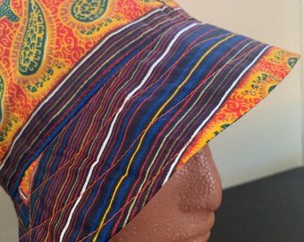 May include: A colorful bucket hat with a paisley pattern in red, yellow, and green. The hat features a striped band with blue, red, yellow, and white stripes. The hat is displayed on a brown mannequin head.