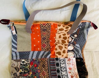 May include: A patchwork tote bag with a variety of fabric patterns and colors, including orange, brown, and blue. The bag has a blue strap and a brown strap, and a zipper closure.